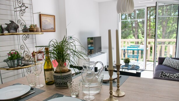 A dining area with a table set for two, a potted plant, wine bottles, and a pitcher. - Apt. Neuf à 50m du Port - Parking Privé, Ascenseur (Saint-Valery-sur-Somme)