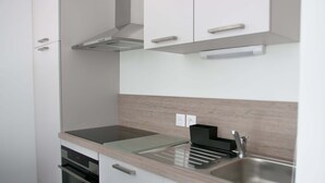 A modern kitchen with white cabinets, a stainless steel sink, and a built-in oven. - Apt. Neuf à 50m du Port - Parking Privé, Ascenseur (Saint-Valery-sur-Somme)