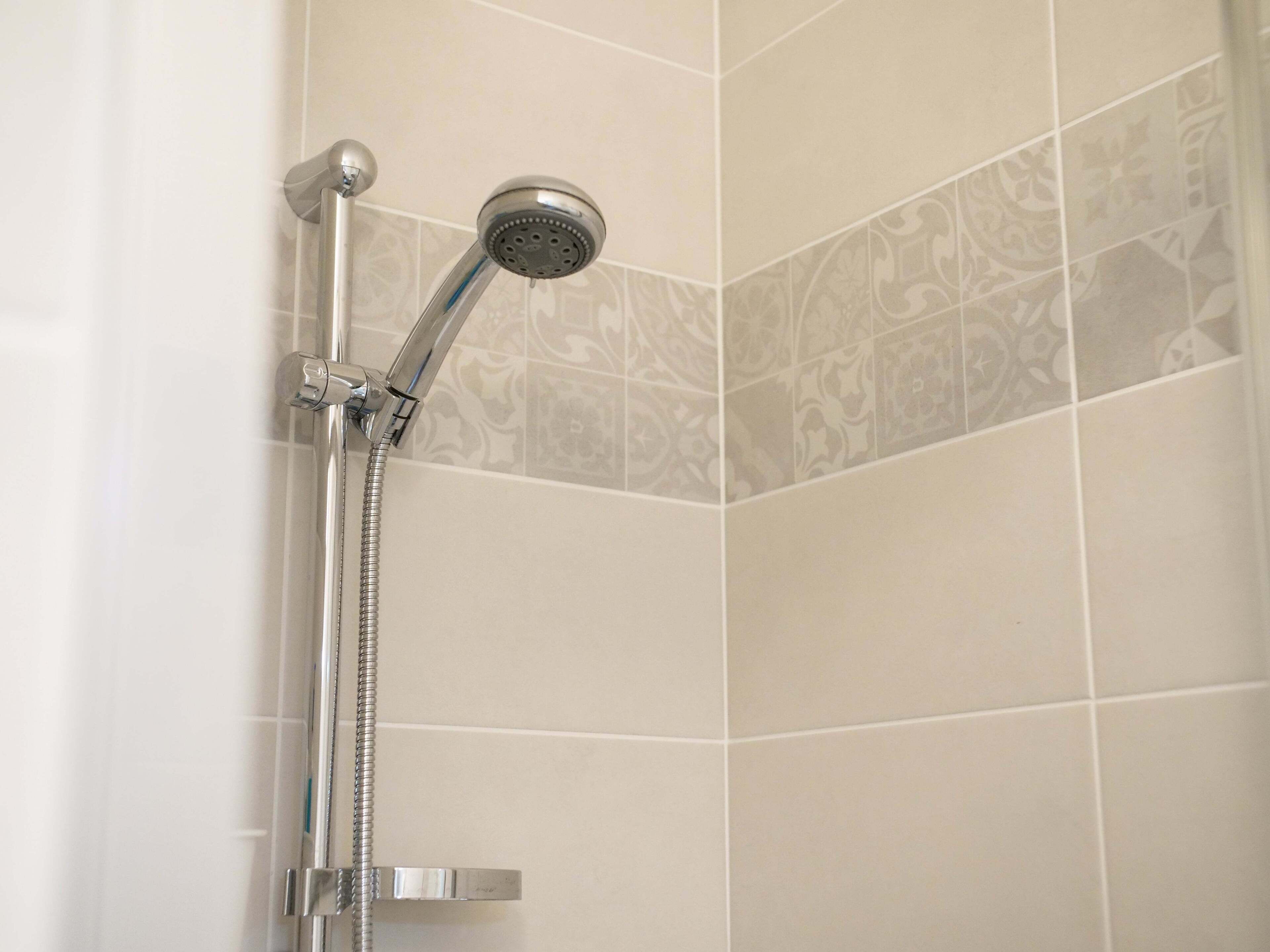 Une douche équipée d’un pommeau de douche à main et d’une pommeau de douche fixe, le tout installé sur un mur recouvert de carreaux décoratifs.