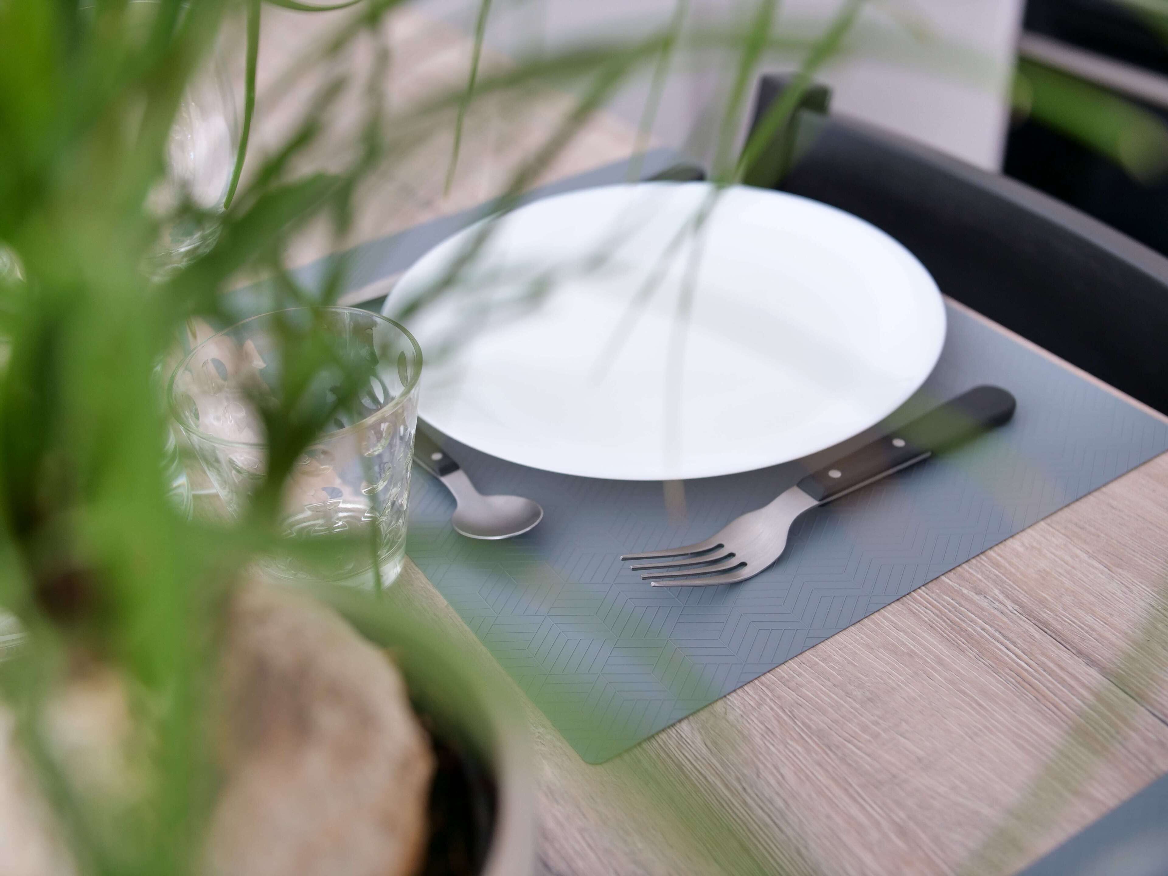 A table set with a white plate, a fork, and a spoon on a green placemat.
