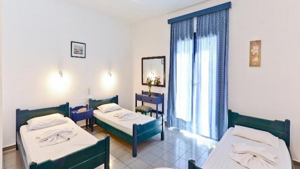 Une chambre d’hôtel avec deux lits simples, une petite table, une chaise, un miroir et une fenêtre avec des rideaux.