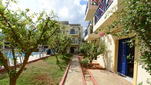 Une cour avec un chemin en pierre, une piscine et un bâtiment aux portes et balcons bleus.