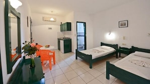Une petite chambre propre, équipée de deux lits simples, d’un bureau, d’une chaise et d’une petite kitchenette.