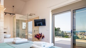 Une chambre d’hôtel moderne dotée d’un balcon, d’une douche à parois de verre et d’un téléviseur à écran plat.