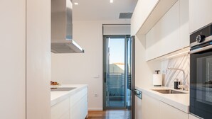 Une cuisine moderne avec des meubles blancs, une hotte en acier inoxydable et un four encastré.