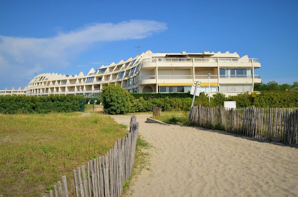 A beachfront hotel with multiple balconies, a sandy beach in front, and a wooden fence.