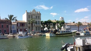 A marina with boats docked, a historic building with a bell tower, and palm trees. - Studio for 2 Adults, Sea & Garden View (Le Grau-du-Roi)