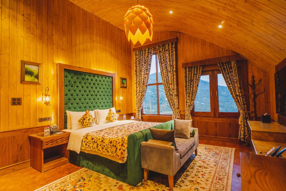 A cozy bedroom with a large bed, a green upholstered headboard, and a wooden ceiling.