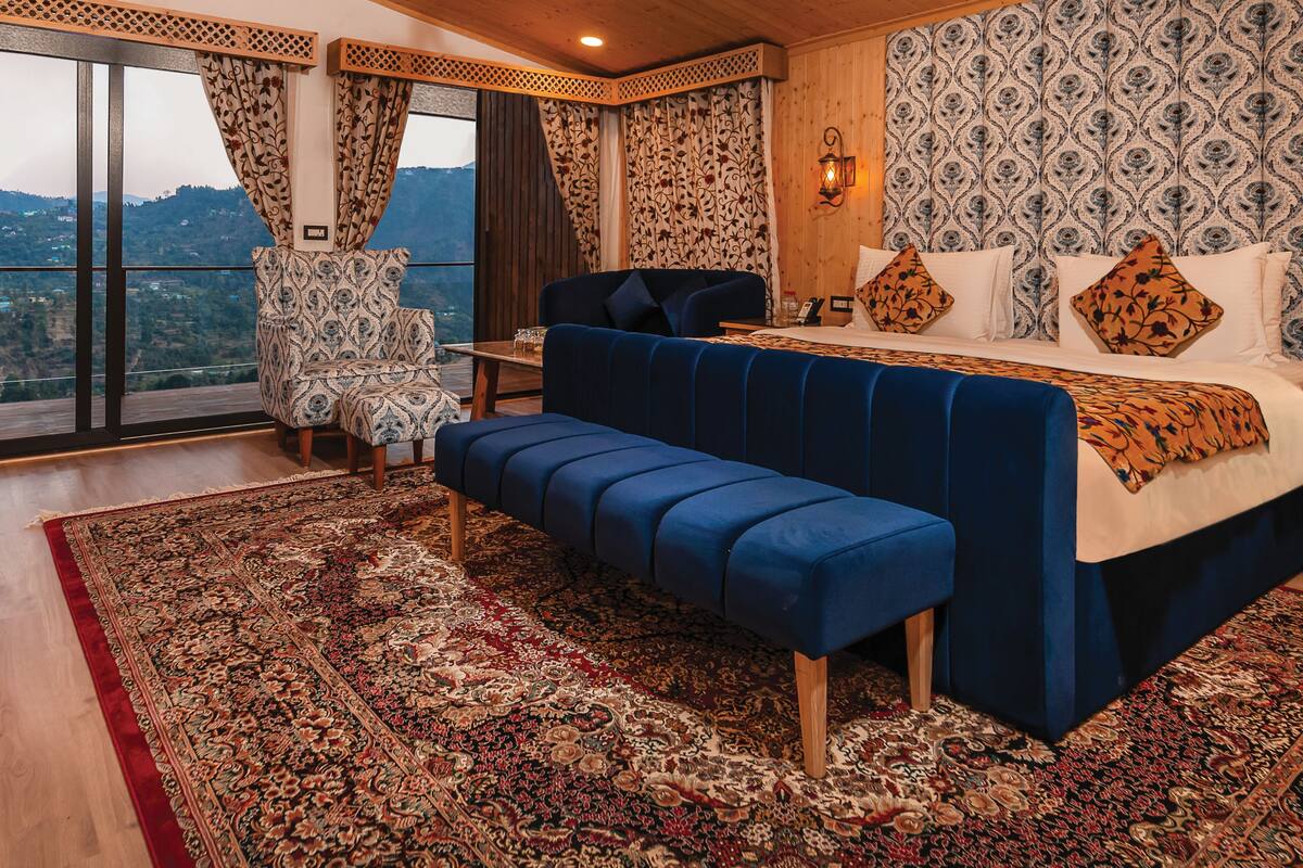 A bedroom with a large bed, a bench, a chair, and a view of the outdoors.