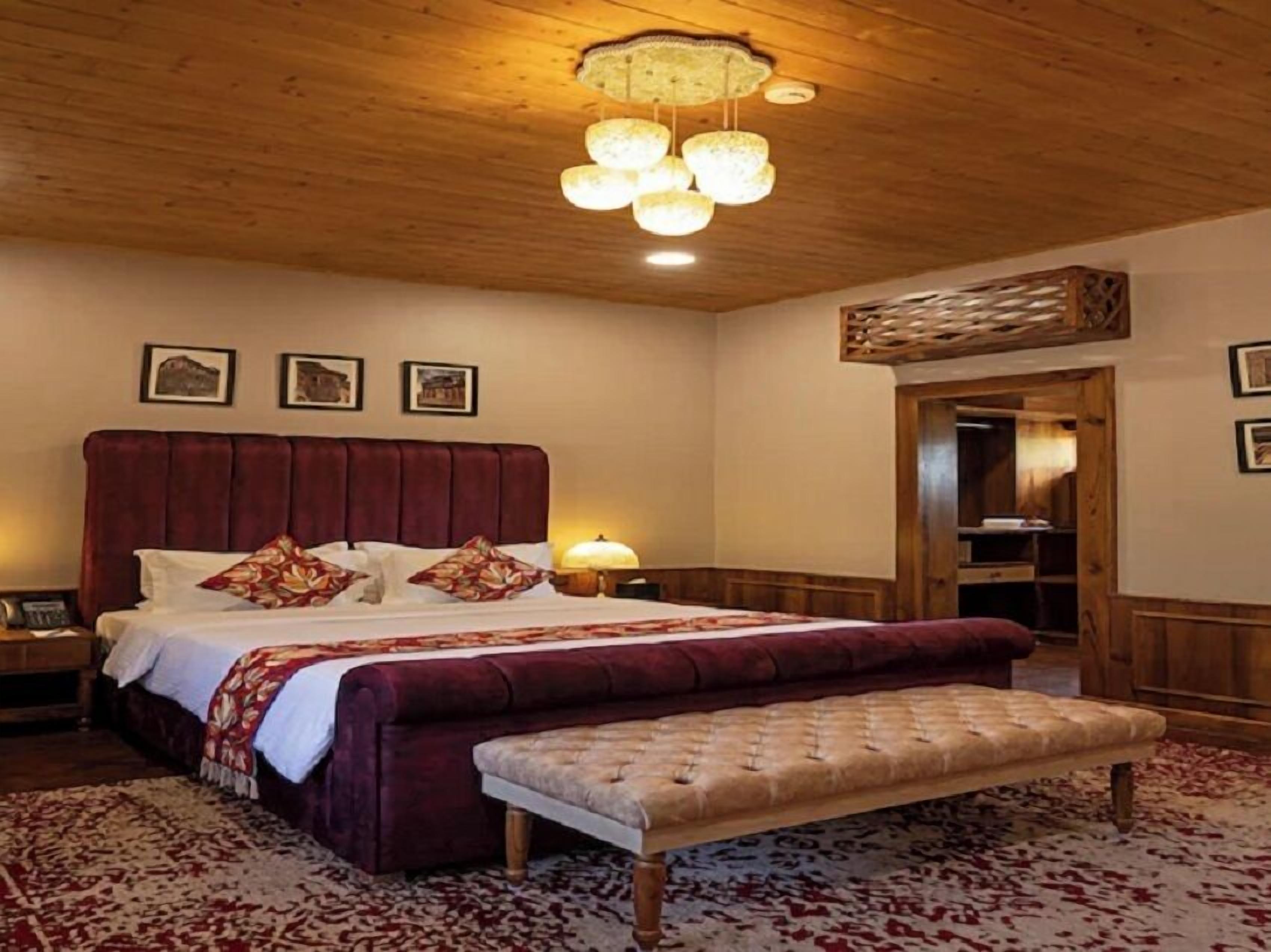 A bedroom with a large bed, a bench, a wooden ceiling, and a nightstand.