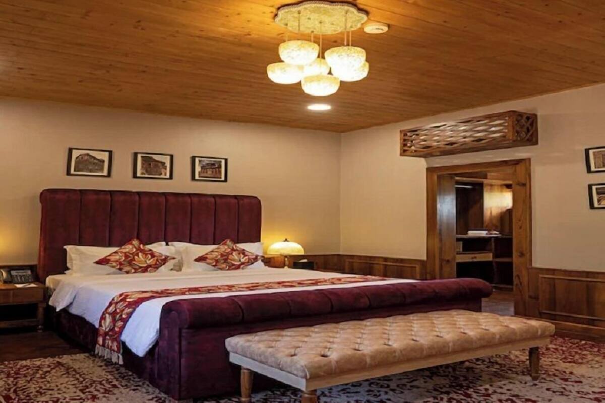 A bedroom with a large bed, a bench, a wooden ceiling, and a nightstand.