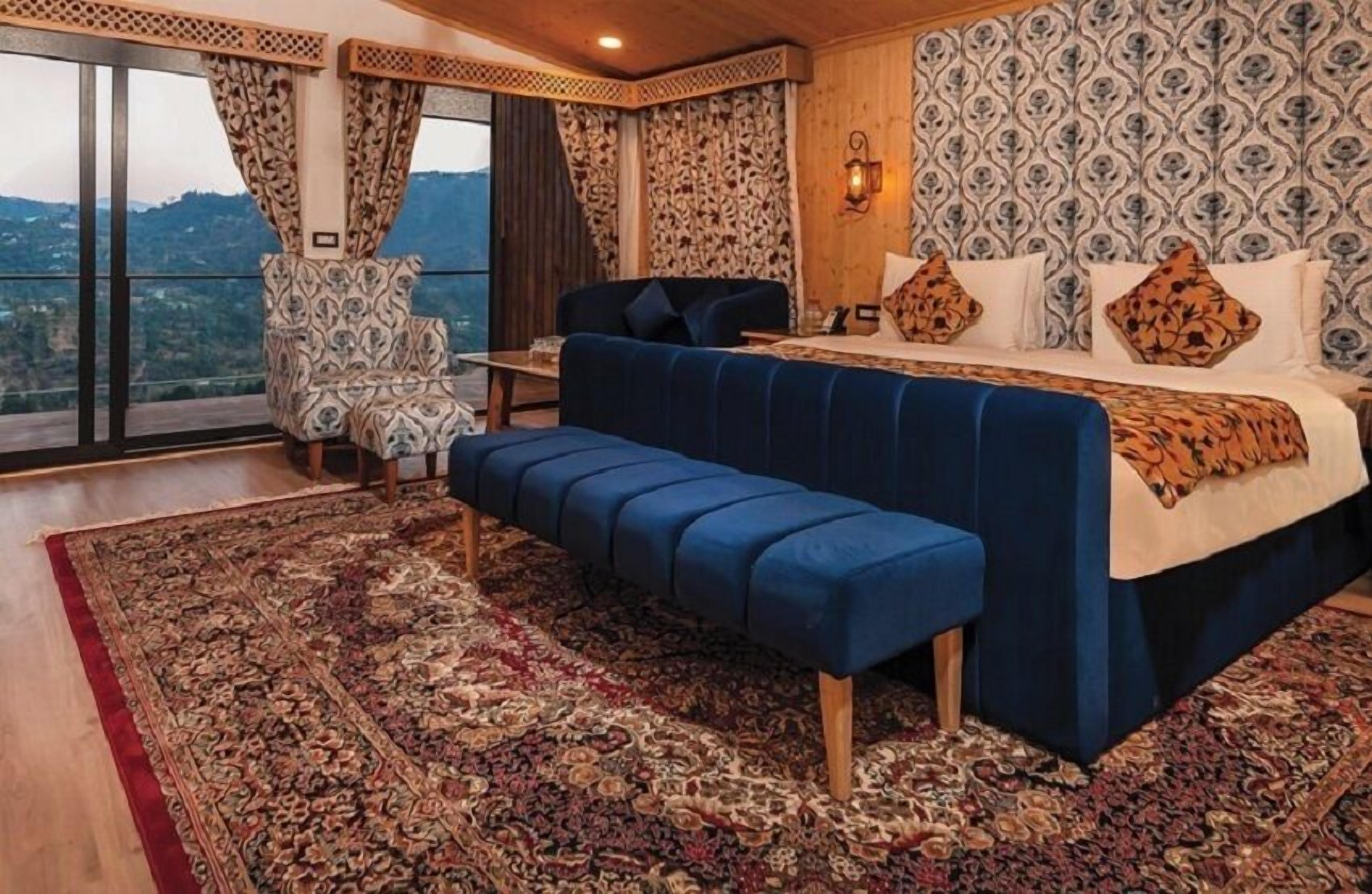 A bedroom with a large bed, a bench, a chair, and a view of the outdoors.