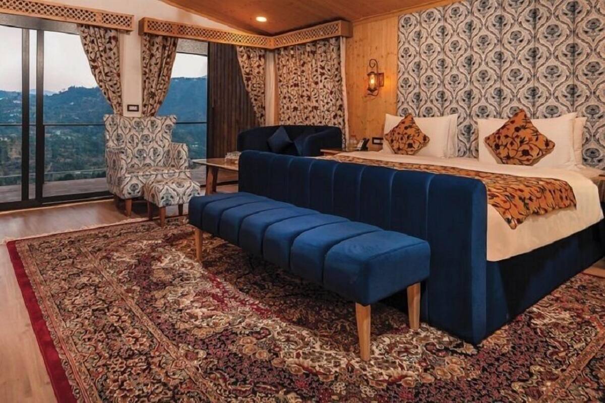A bedroom with a large bed, a bench, a chair, and a view of the outdoors.