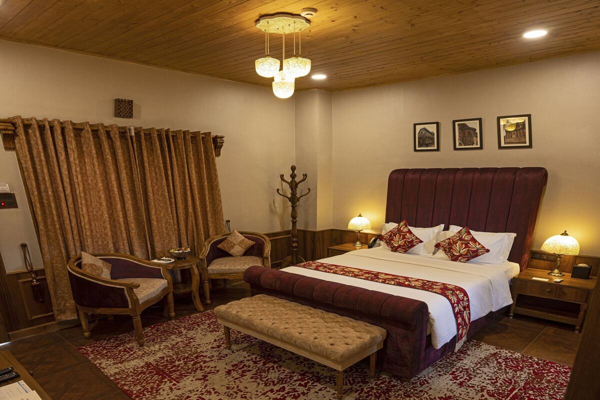 A bedroom with a large bed, two bedside tables with lamps, a bench, a chair, and a wooden headboard.