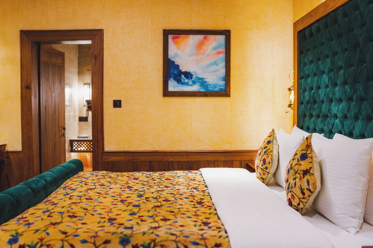 A hotel room with a large bed, floral bedspread, a green upholstered headboard, and a painting on the wall.