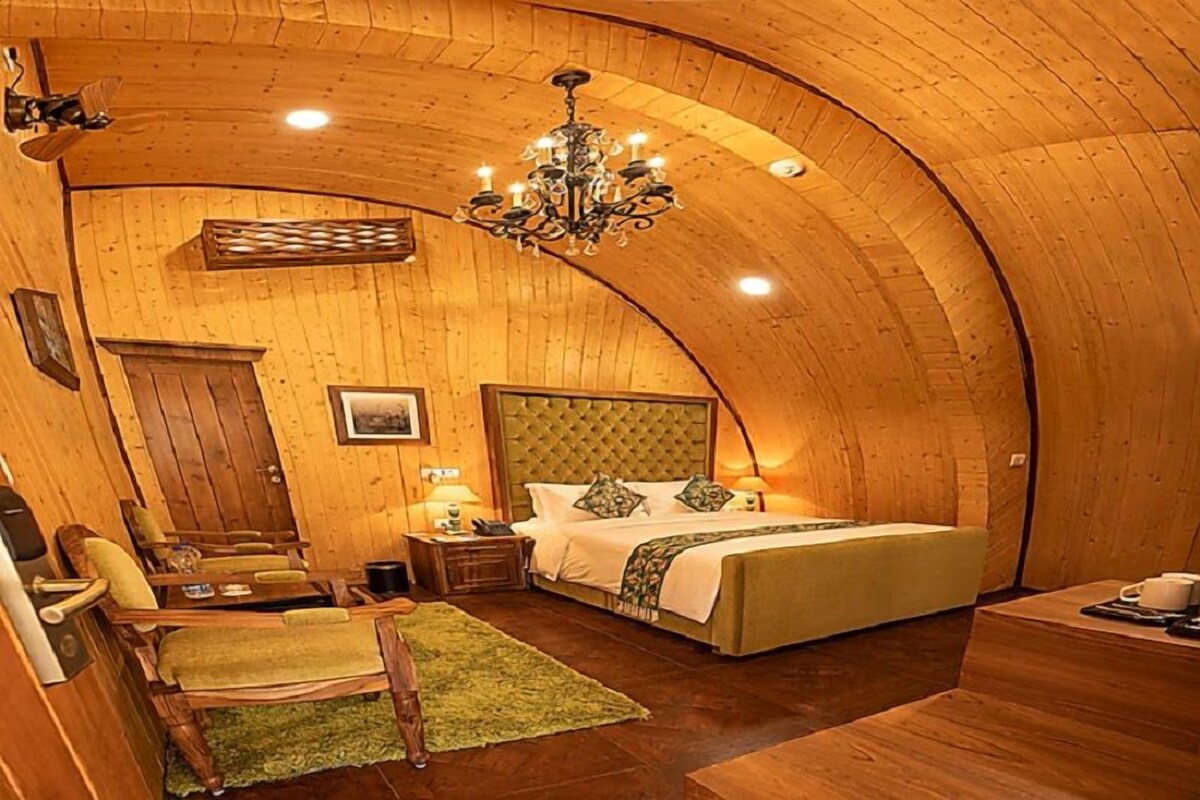 Una habitación acogedora con techo de madera curvada, una cama con cabecera capitonada, una araña y una pequeña mesa con una silla.