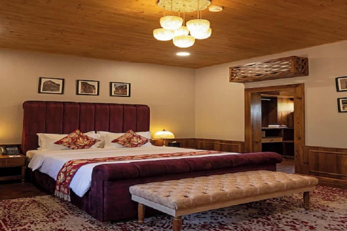 A bedroom with a large bed, a bench, a wooden ceiling, and a nightstand.