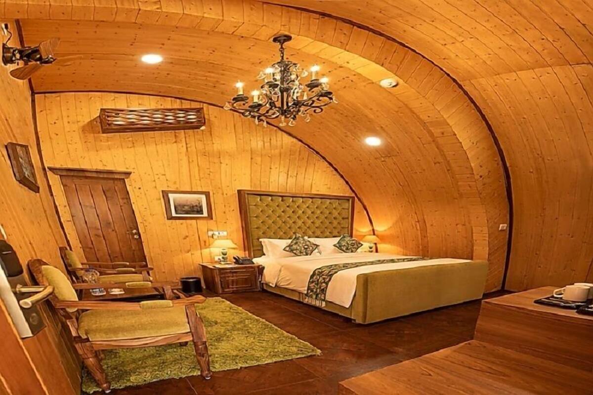 A cozy room with a curved wooden ceiling, a bed with a tufted headboard, a chandelier, and a small table with a chair.