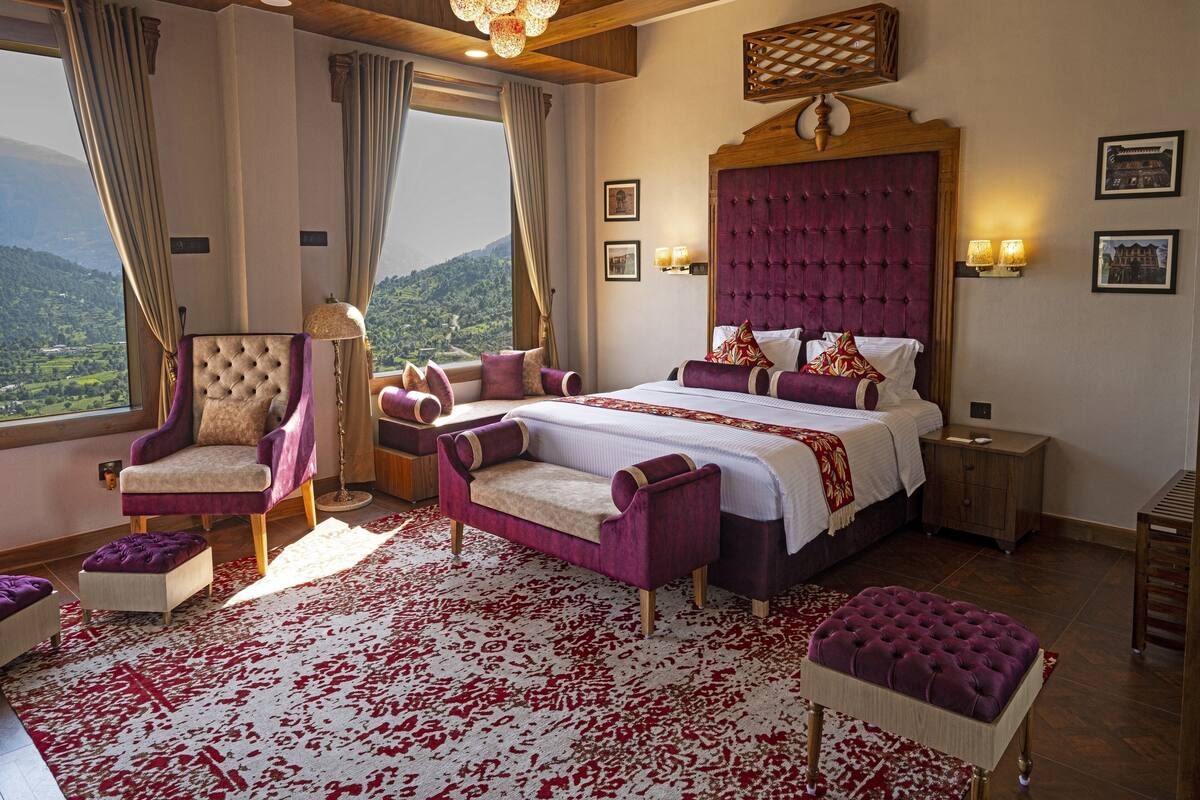 A bedroom with a large bed, a chair, a nightstand, and a view of the outdoors.