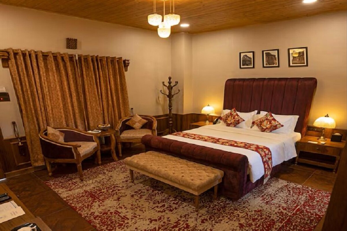 Un dormitorio con una cama grande, dos mesitas de noche con lámparas, un banco de madera, una silla y un perchero.