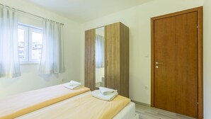 A bedroom with two single beds, a wooden wardrobe, a wooden door, and a window with curtains. - A1 - Spacious apt With the sea View & use of Pool (Podstrana)