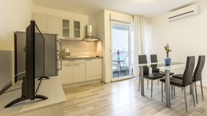 A modern kitchen with a flat-screen TV, a dining area with a glass table and black chairs, and a view through a glass door. - A2 - Spacious apt With the sea View & use of Pool (Podstrana)