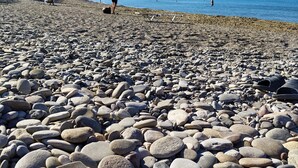 A pebble beach with a clear view of the sea and distant mountains.