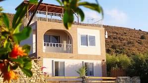 A two-story house with a balcony, stone foundation, and a view of a hilly landscape.