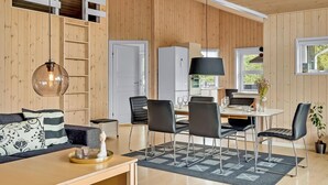 Un intérieur moderne avec un mur lambrissé en bois, un coin repas doté d’une table ronde et de chaises, un canapé agrémenté de coussins à motifs et un luminaire suspendu.