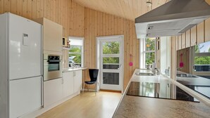 Une cuisine moderne avec des murs en bois, un réfrigérateur blanc, un four encastré, une chaise noire et une grande fenêtre.