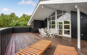 Eine Holzdachterrasse mit Tisch und Stühlen, umgeben von einem schwarzen Zaun und einer Glastür zum Garten.