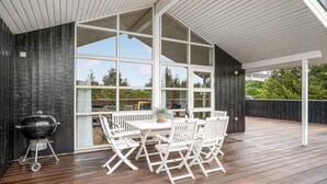 Un patio extérieur couvert avec une terrasse en bois, des chaises pliantes blanches, une table et un barbecue.