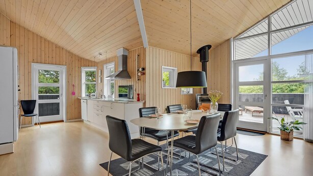 Une cuisine spacieuse avec un lambris en bois, un îlot central et un coin repas comprenant une grande table et des chaises.
