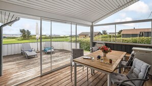 Eine überdachte Terrasse mit Holzboden, einem Tisch und Stühlen sowie Blick auf die umliegende Landschaft.