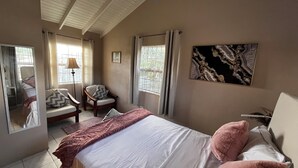 Een slaapkamer met een bed, een stoel, een bureau, een lamp en een schilderij aan de muur.
