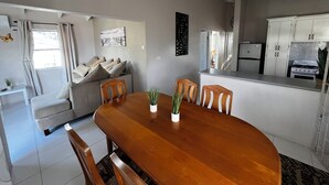 Een moderne woonkamer met een houten eettafel, een grijze bank en een keuken met witte kasten en apparatuur.