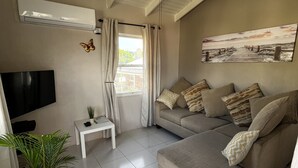 Een moderne woonkamer met een plafondventilator, een flatscreen televisie, een bank met gestreepte kussens, een klein wit tafeltje en een potplant.