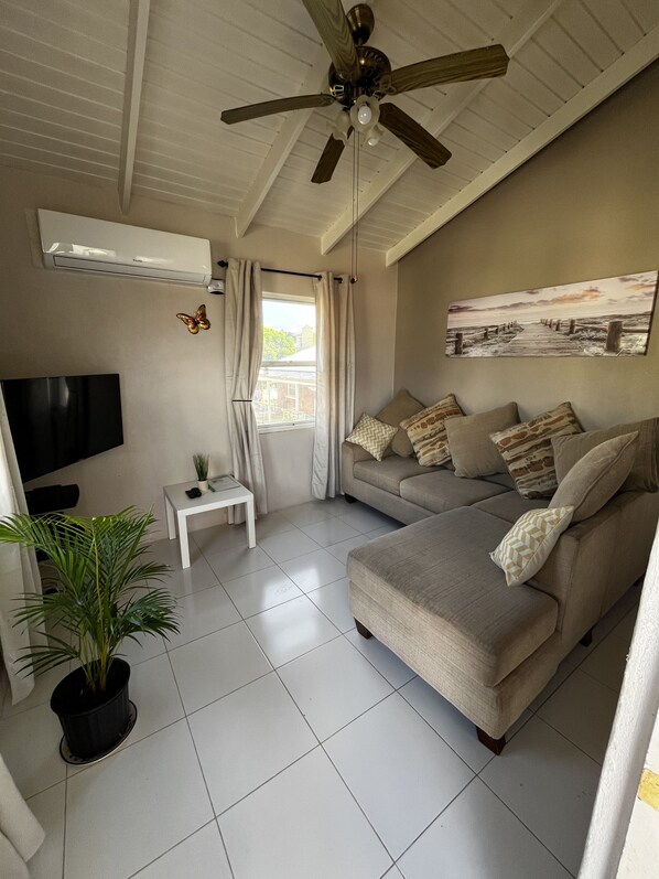 Een moderne woonkamer met een plafondventilator, een flatscreen televisie, een bank met gestreepte kussens, een klein wit tafeltje en een potplant.
