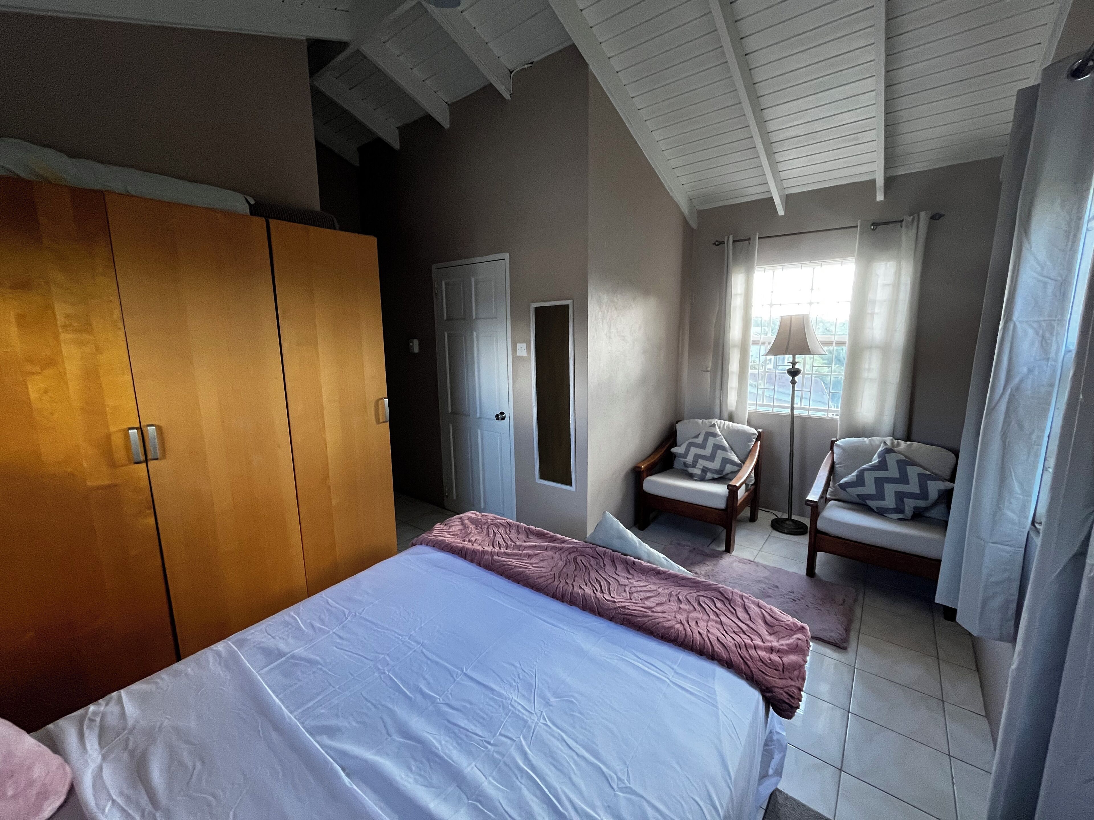 Ein Schlafzimmer mit Bett, Kleiderschrank, Stuhl, Schreibtisch und einem Fenster mit Vorhängen.
