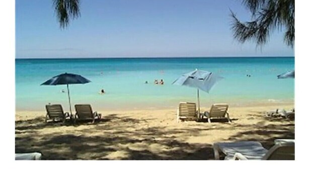 Een strand met twee ligstoelen en parasols, een heldere lucht en de oceaan op de achtergrond.