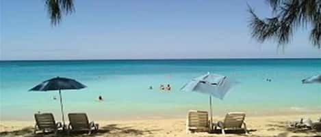 A beach with lounge chairs and umbrellas, a clear sky, and the ocean.