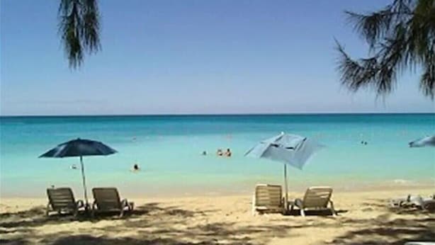 Una playa con dos sillas reclinables y sombrillas, cielo despejado y el océano al fondo.