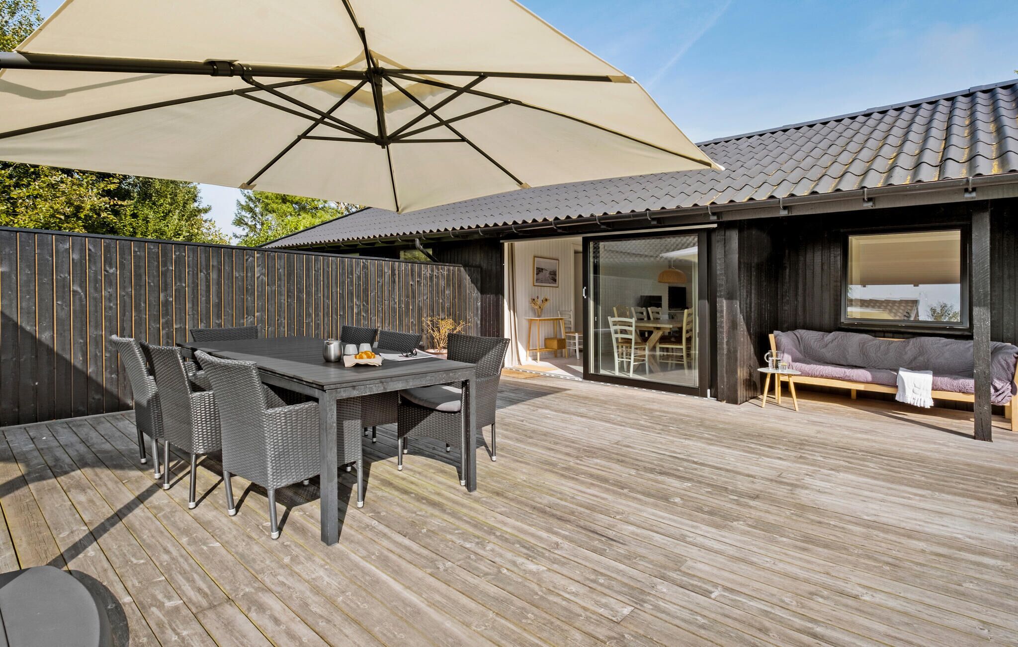 Une terrasse en bois avec une table et des chaises, un grand parasol et un canapé.