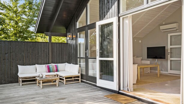 Une terrasse extérieure moderne avec un canapé blanc et des bancs en bois, un téléviseur dans la pièce adjacente et une clôture en bois.