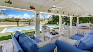 Una terrazza esterna con divani blu, sedie bianche e una piscina.
