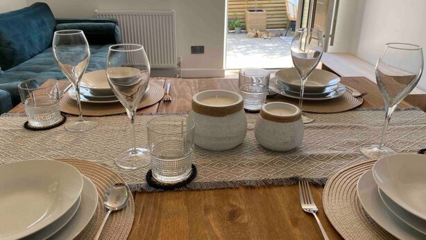 Une table à manger dressée avec des assiettes, des verres et des bougies, donnant sur un jardin et avec un canapé bleu en arrière-plan.