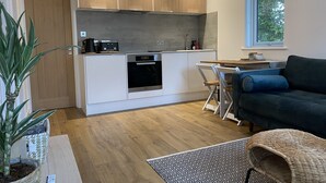 Une cuisine moderne avec des meubles blancs, un four encastré et un coin repas comprenant un canapé bleu et un fauteuil en osier.