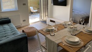 Un salon moderne avec un canapé, une table à manger pour quatre personnes et un téléviseur fixé au mur.