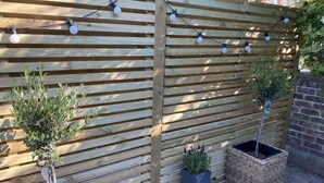 Une clôture en bois décorée de guirlandes lumineuses, de plantes en pot et d'un panier en osier.
