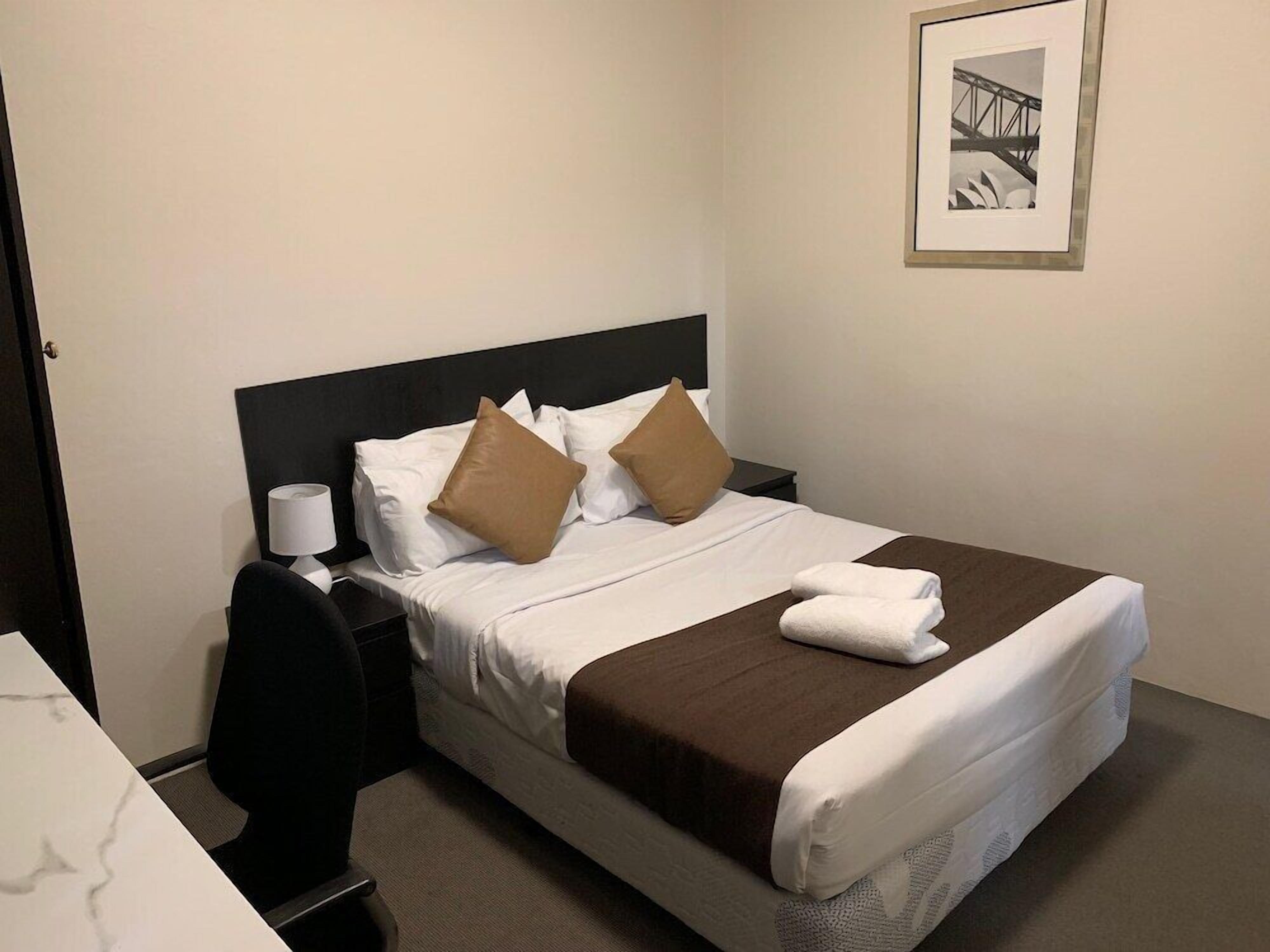 A neatly made bed with white and brown bedding, a black headboard, and a framed picture on the wall.